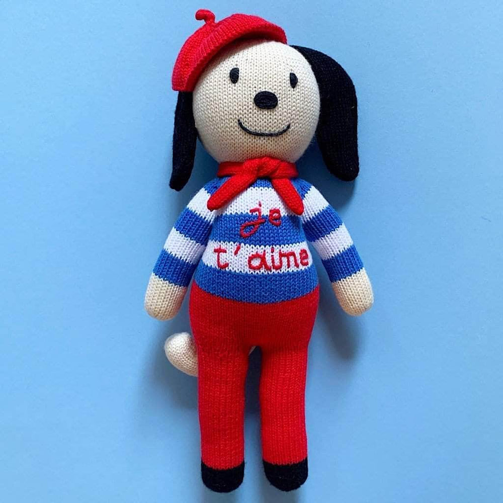 Picture of cream-colored knit dog doll with striped blue sweater, red pants, red beret and red scarf.  The sweater is hand-embroidered with the words "je t&