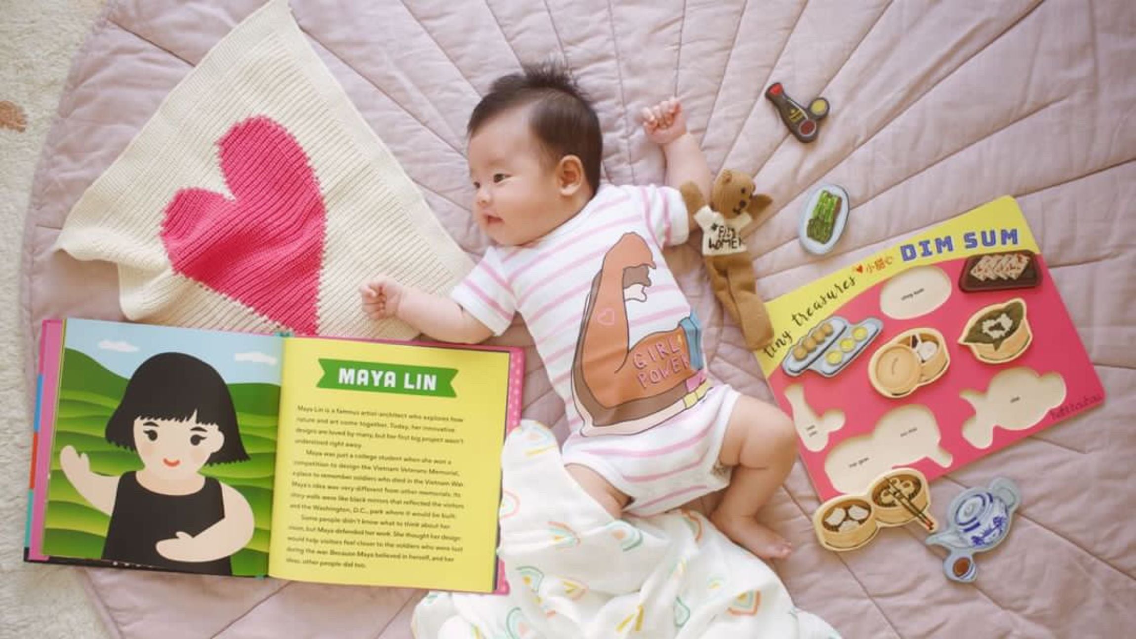 Baby lying with 'girl power' print onesie, toys and a security blanket