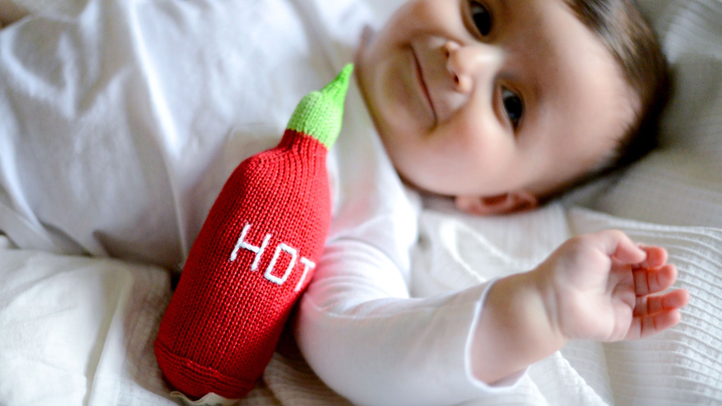 A smiling baby with an organic Hot Sauce baby rattle