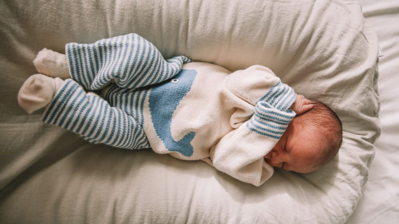 A sleeping baby wearing an organic knitted whale romper with blue stripes