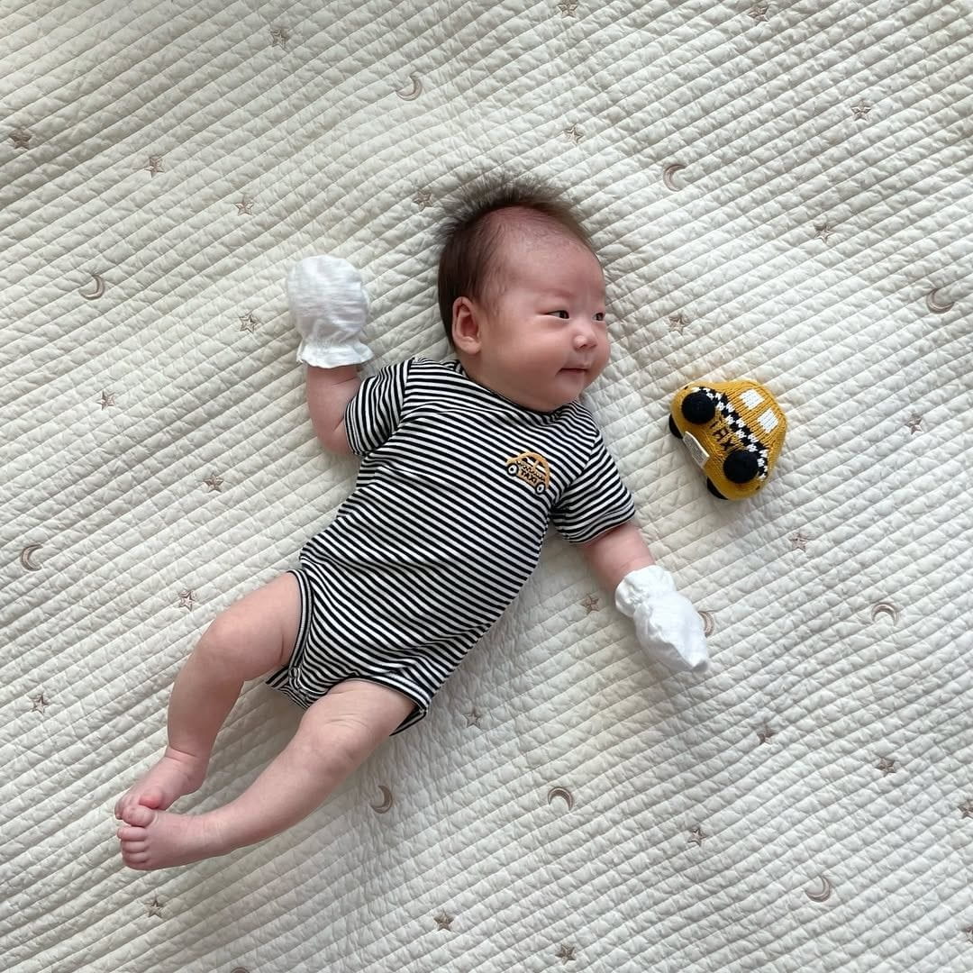 Estella organic cotton baby gift set arranged on a soft cream linen background — bodysuit, knit rattle and swaddle gift-boxed and ready to give in New York City.