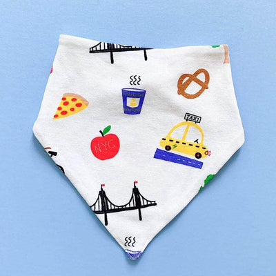 Triangular baby bib that snaps in the back. Features a white background with small images of pretzels, apples, hotdogs, pizza, trees, coffee, taxis, bikes and bridges. 