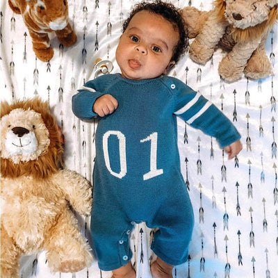 Baby, in his crib and surrounded by his stuffed animals, wearing the blue knitted Estella 01 romper with two varsity stripes on each sleeve. The romper is french blue with "01" and stripes intarsia in white.