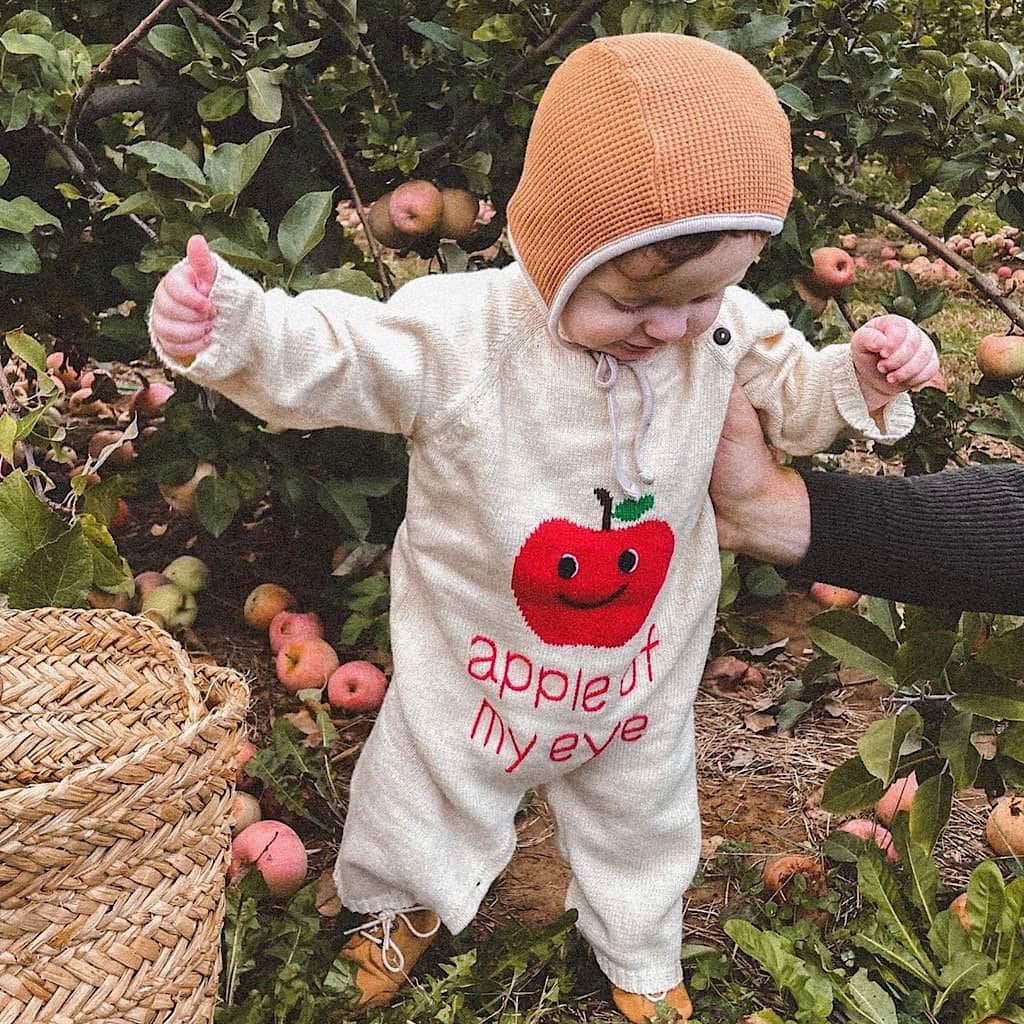 Baby, standing by an apple tree, wearing the "Apple of my Eye" romper