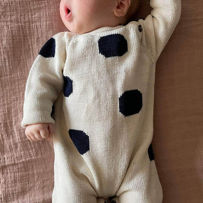 Baby with perfectly chubby cheeks, lying on a clay-colored linen sheet, wearing the cream with scattered large navy dotted romper.