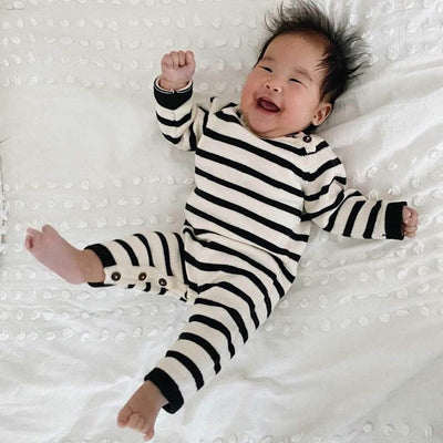 Laughing baby wearing the organic black and cream striped knitted baby romper lying on a white nubby sheet.