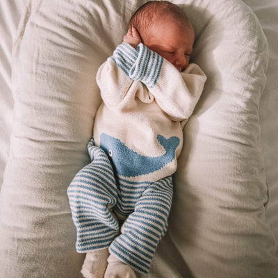 A newborn baby wearing the cream and blue whale romper, soundly sleeping.