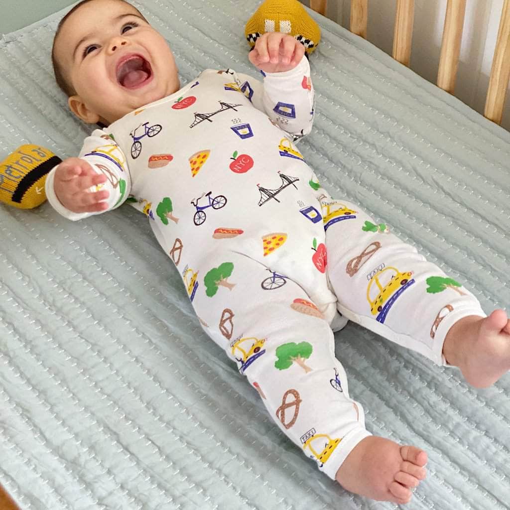 Happy baby in his crib wearing the all over, multi-colored NYC printed long romper. 