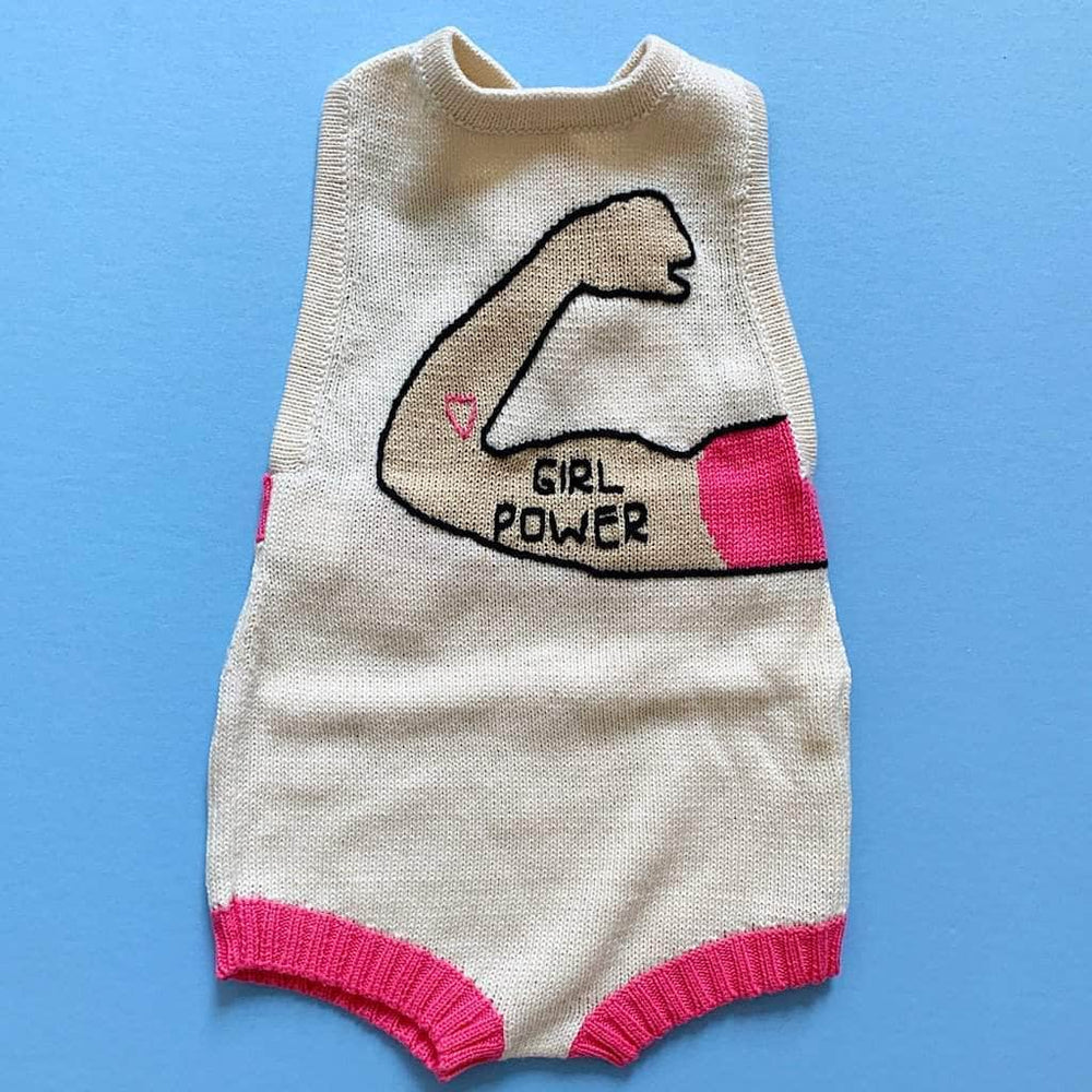 Girl Power baby romper in cream and bright pink with an arm making a muscle. On the arm is a pink heart and the words "Girl Power." The leg holes have pink ribbing. Photographed on a vivid blue background.