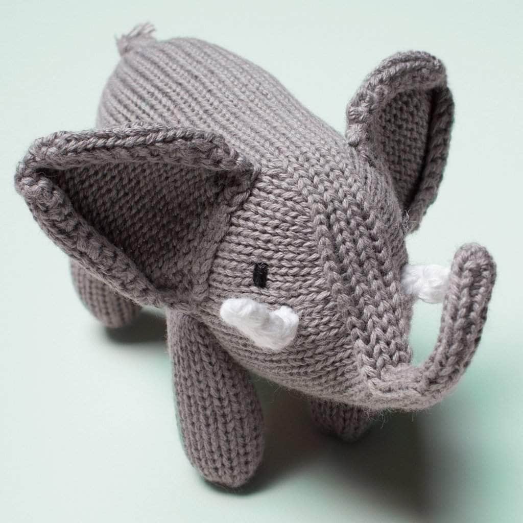 Knitted gray elephant rattle with a large trunk and white knitted tusks.  Photographed on a soft blue background.