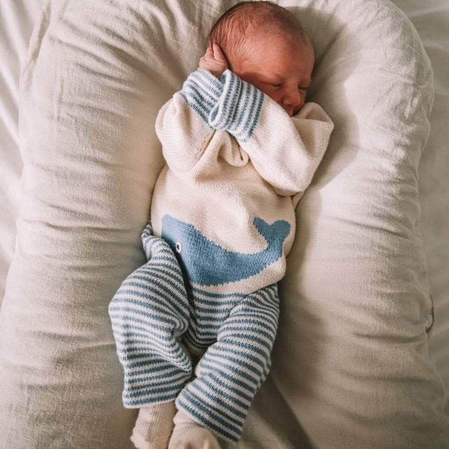 A newborn baby wearing the cream and blue whale romper