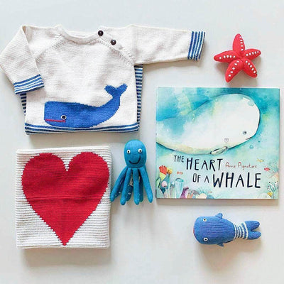 Beautiful 6 piece baby gift set which includes a turquoise octopus, blue whale and red starfish rattles, a blue and cream whale baby romper, a red heart lovey and a hardcover copy of the children's book, "The Heart of a Whale." This is all photographed on a soft gray background.