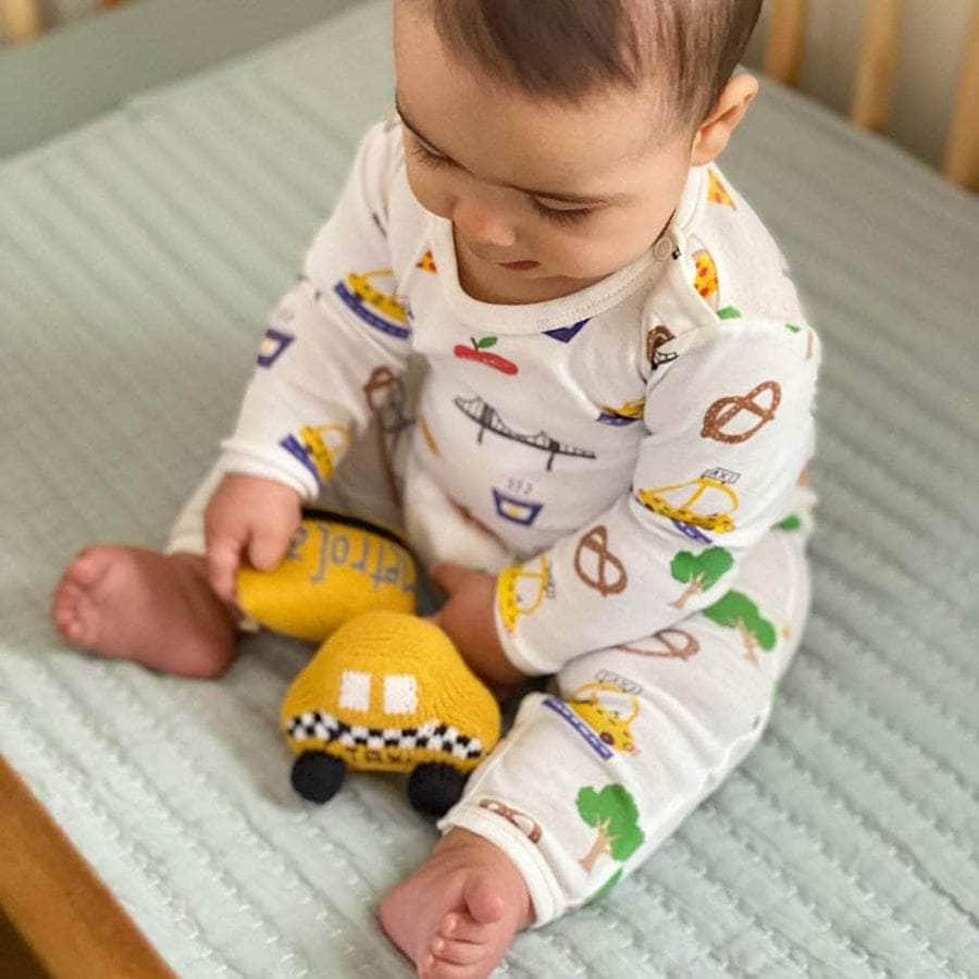 Baby, in his crib, playing with yellow taxi and metro baby rattles 