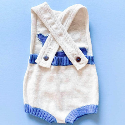 Back of whale romper showing criss-cross straps with 3 button holes and buttons to fasten. Back of romper is ribbed with french blue yarn right above the diaper. Back is otherwise bare. Photographed on a bright blue background.