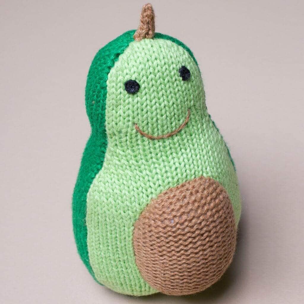 Soft baby toy rattle shaped like an avocado with a dark green back and a lighter green front, smiling face and brown round intarsia on the stomach resembling the pit.