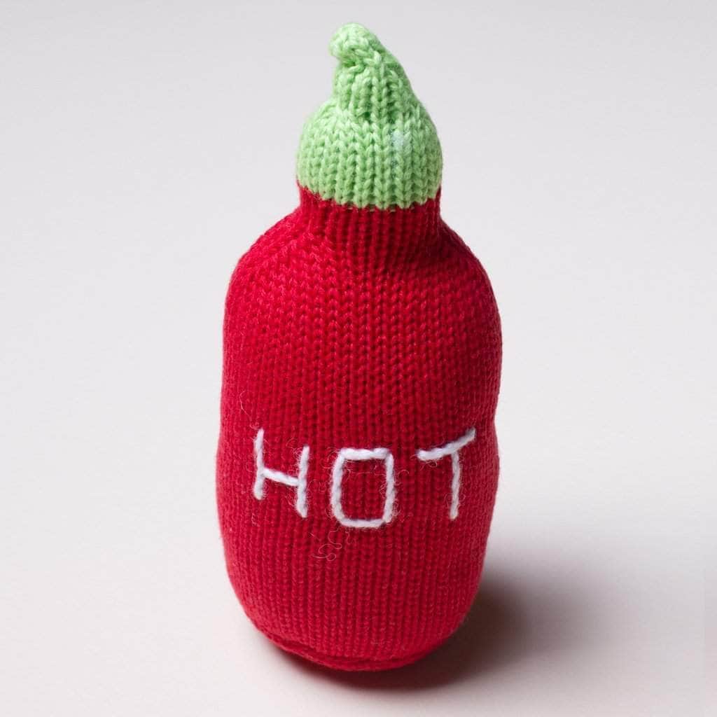 Organic baby rattle toy in the shape of a hot sauce bottle. The bottle is red, the top is green and the word "Hot" is stitched on it in white.