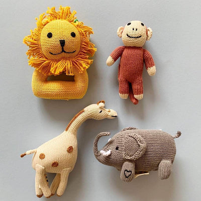 Baby gift set. Photo of four knitted toys: brown monkey rattle, cream giraffe rattle, gray elephant rattle and yellow lion rattle on a soft blue background.