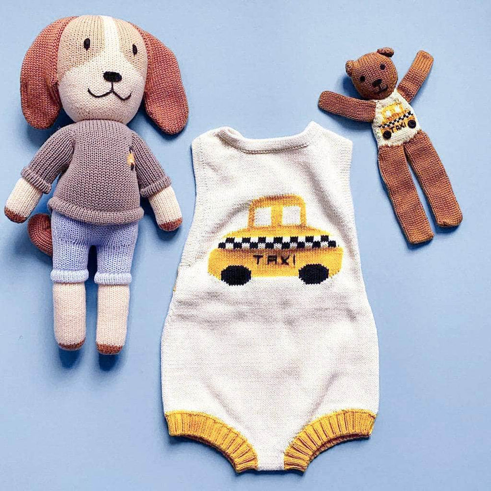 Photo of knitted dog doll with a gray taxi sweater and blue pants, cream knitted baby sleeveless romper with yellow taxi and a brown knitted bear wearing a small version of the knitted taxi baby romper. Shown on a bright blue background. 