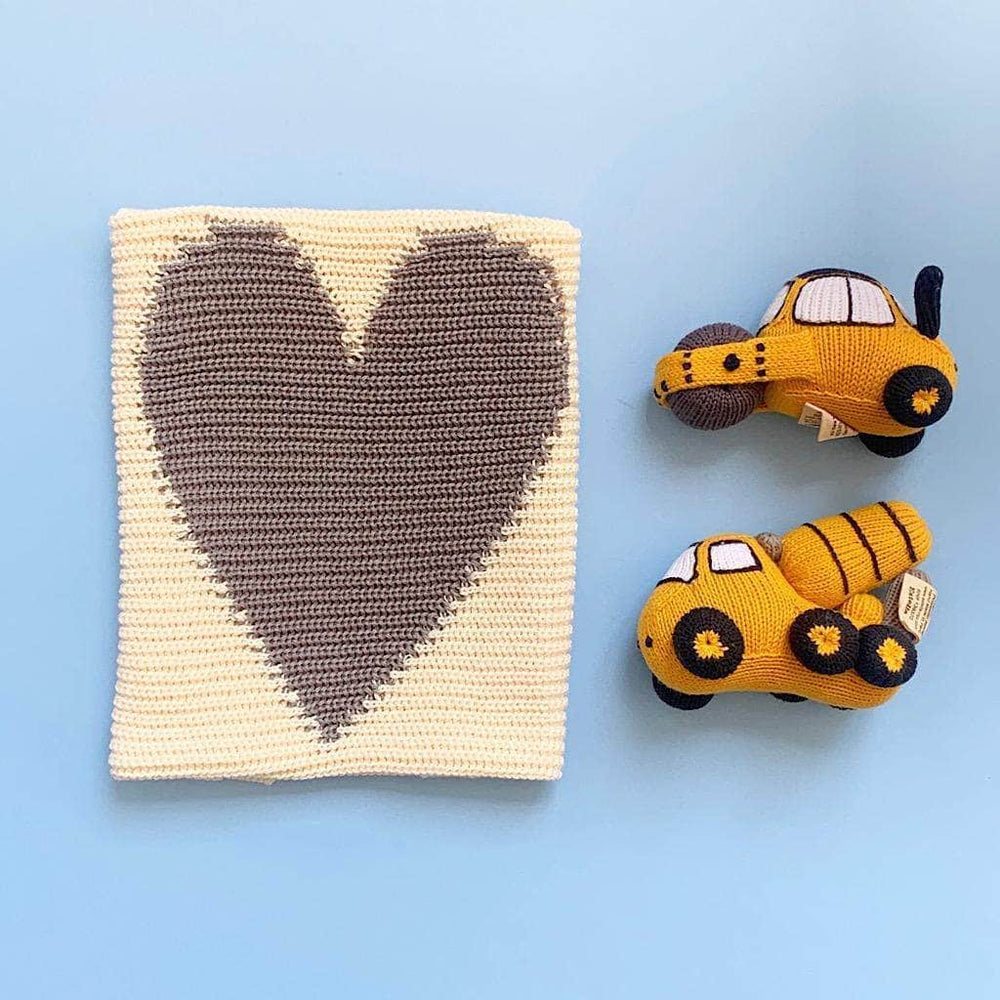 Image of cream baby blanket with gray heart, a bright yellow mixer rattle with black and gray details and a bright yellow roller rattle with black and gray details. Photographed on a soft blue background.