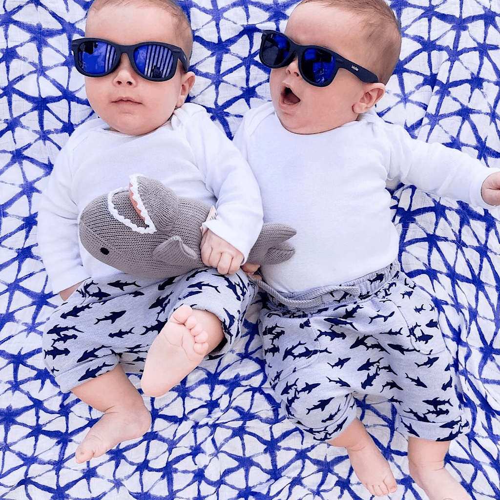 Twin babies wearing sunglasses and shark pants holding the Estella shark pillow toy