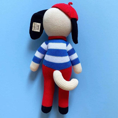 Back of the knit dog doll showing his white tail peaking out of his red pants.  Photographed on a bright blue background