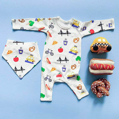 NYC Baby gift set with taxi, hot dog, pretzel rattles and "Big City" baby romper and matching bib. Photographed on a bright blue background. 
