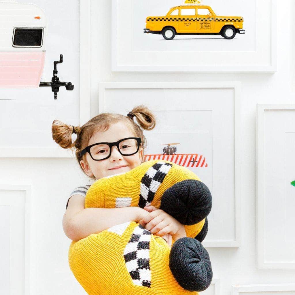 Six year-old girl hugging the large, organic stuffed taxi toy. Taxi is bright yellow with white and black checkered sides and black wheels.
