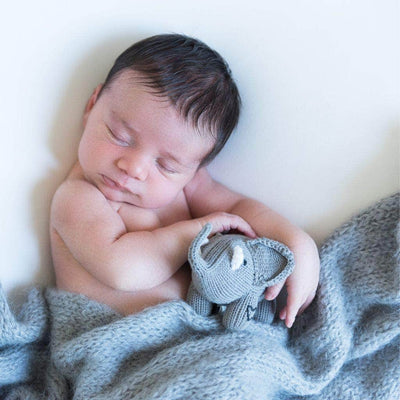 Baby elephant toy in newborn baby's arms. Shows grey rattle toy with black heart stitch.